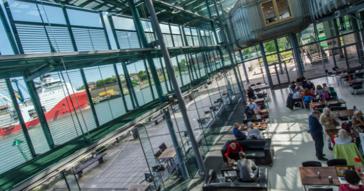 View inside The National Glass Centre, Sunderland, with boat passing by window and people sat eating food.